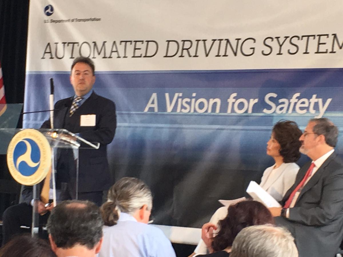 President Riccobono stands at a podium while Secretary Chao and University of Michigan President Schlissel sit off to the side.