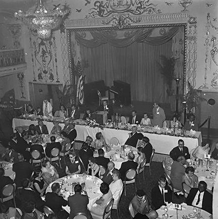 View of the convention stage and Kenneth Jernigan at the podium. Banquet tables full of Federationists occupy the foreground of the photo.