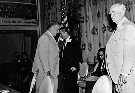 Congressman Walter S. Baring stands on stage with his back to the audience. His assistant, Tim Seward, stands in the right side of the photo.