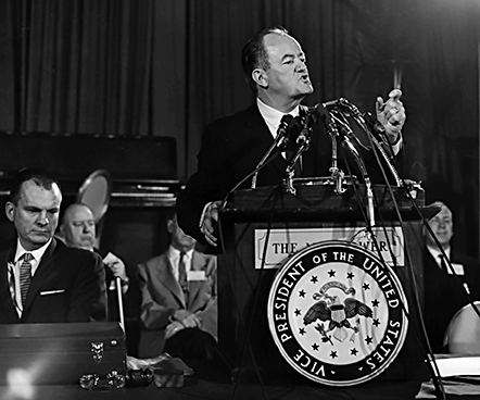 Vice President Hubert H. Humphrey stands at the convention podium, which bears the seal of his office.