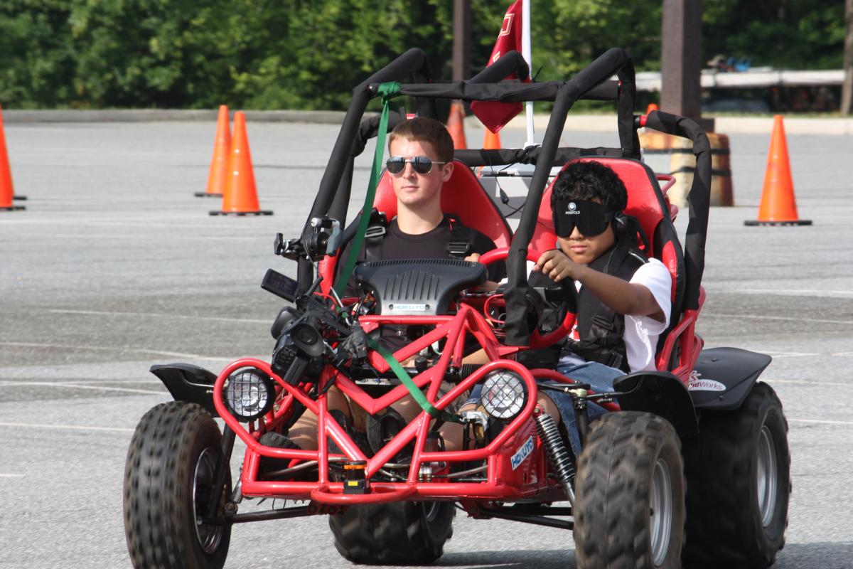 A student drives a dune buggy while under sleep shades at the NFB Youth Slam.