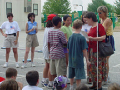 Mrs. Maurer addresses students, parents, and teachers following the presentation of the check to the NFB.  The seven youngsters who raised the most money are clustered around Mrs.  Maurer.
