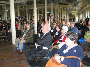 Fair attendees are seated at the south end of the third-floor space at the National Center for the Blind to hear remarks from President Maurer and others.   Honorary fair marshall William Donald Schaefer (center) listens intently.