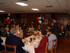 Amid red, white and blue balloons, Governor Ehrlich (standing) addresses luncheon attendees.   Pictured with him from left to right are John Busher, chair of the NFB Research adn Training Institute policy advisory board; Patricia Maurer; and Bill Streuver and Jim Brinkley, cochairs of the institute's grand opening celebration.