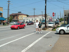 Two women under sleepshades are crossing a street using long white canes.