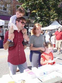 A young family stops to talk with volunteers at an NFB information table.  The chidren check out NFB Braille alphabet cards.