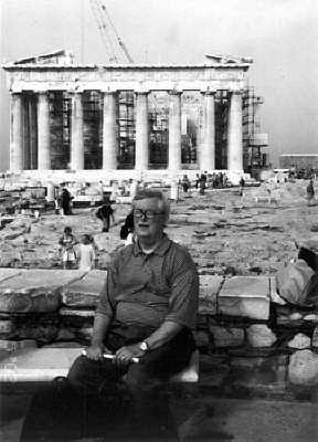 Bob Gardner sits on the Acropolis with the Parthenon visible behind him.