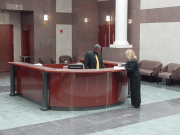 The reception area in the fourth-floor atrium. Here a guest signs in while the receptionist, Mr. Branch, looks on from behind his horseshoe-shaped counter. The entrance to Members Hall is visible in the upper left corner. The hallway to President Maurer�s office can be seen leading off to the right.