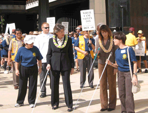 NFB of Hawai�i member Brook Sexton (far right) instructs Hawai�i Governor Linda Lingle (center) and Department of Human Services Director Lillian Koller (left) in travel techniques using the long white cane.  Both officials joined the march of more than 150 blind Hawai�ians and supporters through downtown Honolulu as part of White Cane Safety Day.