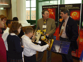Two men stand in front of the display as a group of children check it out.