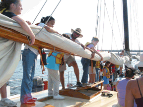 BISM students hold the mainsail down so that it can be lashed to the boom.