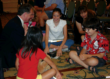 NFB President Marc Maurer sits on the floor with the blind kids attending the opening session of the National Organization of Parents of Blind Children annual seminar. He is preparing to teach them how easy it is to use the Kurzweil�National Federation of the Blind Reader.