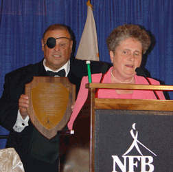 Ramona Walhof reads the text of the plaque while Charlie Brown stands behind her holding it.