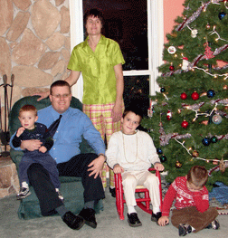 The Wenzel family: Dan seated with Tanner in his lap; Jennifer, standing; Roland, seated in a rocking chair; and Stephen seated on the floor, not very happy about having his picture taken