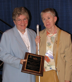 Sister Meg Fleming and Sharon Maneki holding her award stand together on the platform.