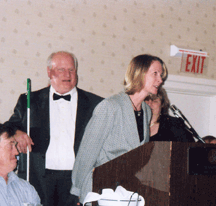 Carrie Thompson speaks to the banquet audience at the NFB of Iowa convention after receiving the charter for the parents of blind children division. NFB of Iowa President Michael Barber looks on.