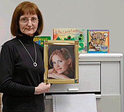 Debra Bonde poses with a photograph of her daughter Anna in front of a Seedlings Braille embosser. Two print/Braille children�s books are visible on top of the embosser.