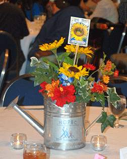 We can see silk flowers and a packet of flower seeds in a small watering can.