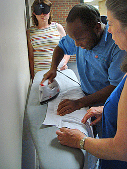 Shelley Bruns teaches Carry Joanis to iron a shirt while Beth Allred waits her turn.