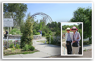 Lela Isaacs (left) and Marjorie Jean arrive at the Legacy Garden prepared to do some weeding. They are standing to the right of the arbor at the entrance. Behind them is the circular raised bed that is the garden&rsquo;s focal point.