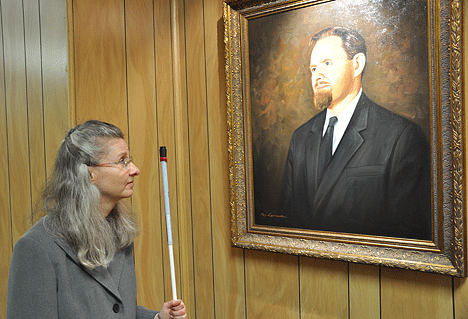 Lou Ann Blake, tenBroek Disability Law Symposium coordinator, examines the newly hung portrait of Dr. Jacobus tenBroek just outside the auditorium in the NFB Jernigan Institute.
