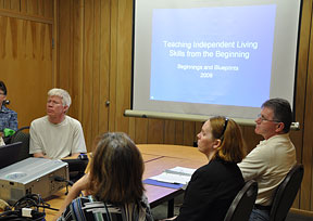 (Left to right) Rick Trimble, an unidentified participant, Patricia Chichester, and Robert Palermo sit together at a parents breakout session during the conference. In the background the conference name is visible on a video screen.