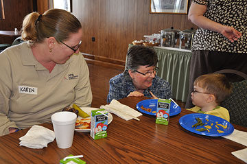 Karen Zakhnini, education project manager with the NFB Jernigan Institute, talks with one of the children attending the Beginnings and Blueprints Early Childhood Conference over lunch in the dining room at the National Center for the Blind. Dinah Little, Institute director of education, kneels beside their table to join the conversation.