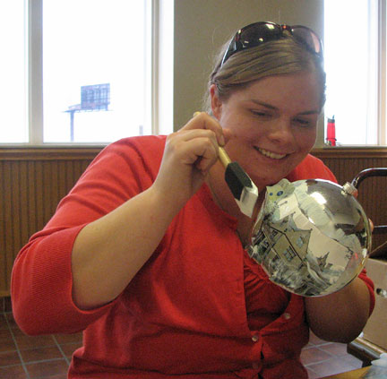 Natalie Shaheen uses a paint brush to apply glue to a tree ornament.