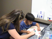Alvin is making puff ball Braille cards. In the photograph he is working with BELL instructor Jackie Otwell to count out the appropriate number of puff balls to make the letter "D."