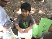 Mao, another student from the NFB of Georgia BELL program, had a birthday during the two-week session. His friends made him Braille birthday cards. Mao sits at a picnic table next to Paul Howard, BELL instructor, reading his cards.