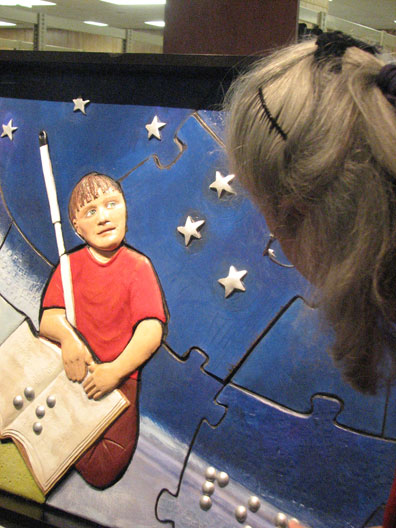 A close-up of the boy in the mural reading a Braille book