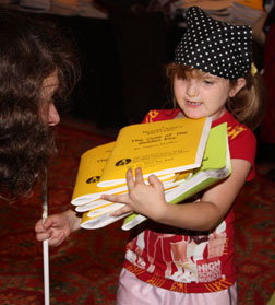 At the Braille Book Flea Market, Anna Walker holds her cane in one hand and a stack of six Braille volumes with the other, balancing the books with her chin.