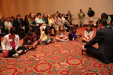 NFB President Marc Maurer sits on the floor talking to a circle of attentive children.