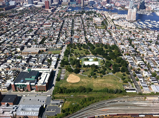 This aerial photograph of part of South Baltimore shows railroad tracks in the foreground, row houses and neighborhood shops, then Federal Hill, and at the top the skyscrapers of downtown.  The most prominent feature in the foreground is the National Center for the Blind, covering an entire block, beside Riverside Park.  We can see the south face of the Jernigan Institute on Wells Street.  Byrd Street can be seen on the west side of the Institute.  Embracing the JI are the two wings of the NFB�s original building, one along Johnson Street on the east and the other along Barney Street on the north.