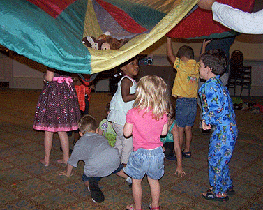 Children play tag under a parachute.