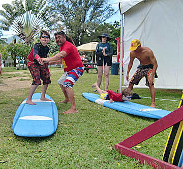 Uncle Mitch and Ke'ale teach Vejas and Petras how to transition to proper surfing stance during the land portion of the lesson while Rasa looks on.