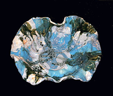 Shown here is a large, free-form bowl with edges fluted like an open flower. It is glazed with celadon and is transparent green and Acapulco blue with a deeper blue wash over all. The bowl has a light, airy appearance, but it is so large that it took three people to apply the glaze�two to hold the bowl while potter Lynda Lambert applied the glaze.