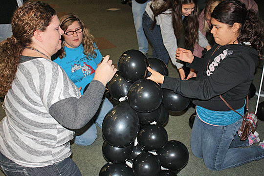 Three girls build a balloon tower using lots of masking tape.