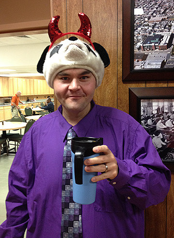 Nick Lambright salutes the camera with his coffee, while wearing on his head a unique hat, a panda with devil horns.
