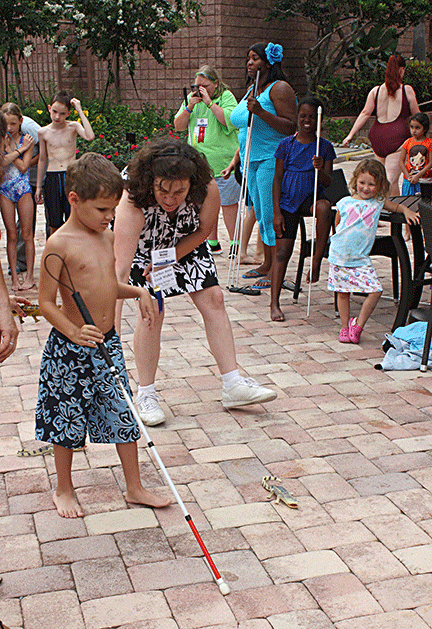 Nick Oliver uses his cane to navigate around plastic alligators on the cobblestones around the pool as part of the Breaking Barriers Triathlon.