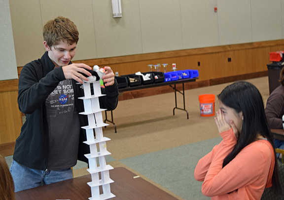 Jamison Hunter balances a small plush panda on tower of eight notecards as Kristie Hong watches in fear of tower collapse.