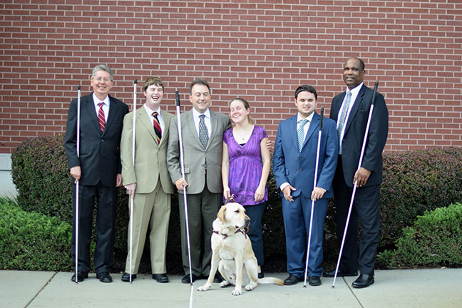John Par&eacute;, Michael Ausbun, Mark Riccobono, Julie McGinnity with her dog guide Bill in front of her, Jerad Nylin, and Anil Lewis pose together in front of the Jernigan Institute.