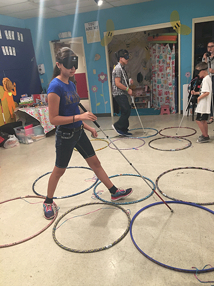 Both wearing learning shades and using their canes, EvaMaria plays Braille Twister against Isaac.