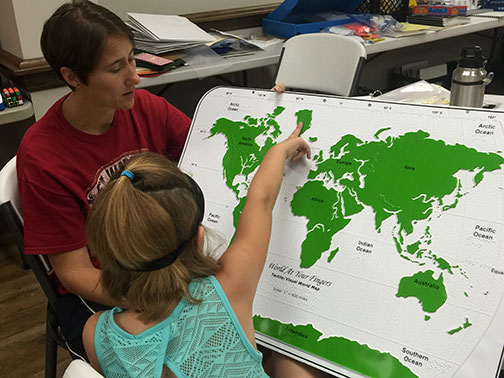 Karli learns latitude and longitude using a tactile world map while wearing her learning shades.