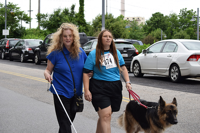 One runner, her guide, and their dog approach the finish line