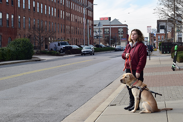 Ashley Alvey stands by the road with her guide dog