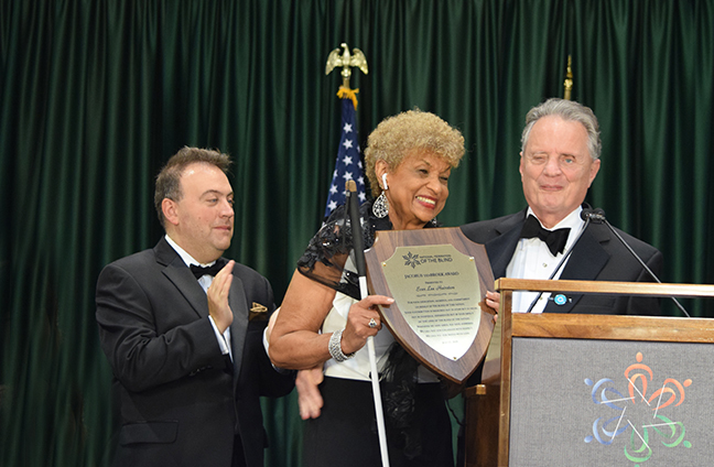 Ever Lee Hairston smiles as she holds up her plaque. Marc Maurer and President Riccobono smile and clap beside her.