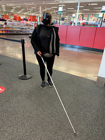 Katie Carmack (wearing training shades and with her long white cane) at a Target store for her orientation and mobility class