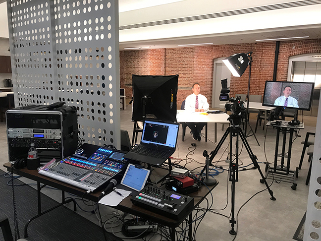 A view of the Presidential Release recording studio. The recording equipment is in the foreground with the lights and camera in front and President Riccobono at a table near the back.