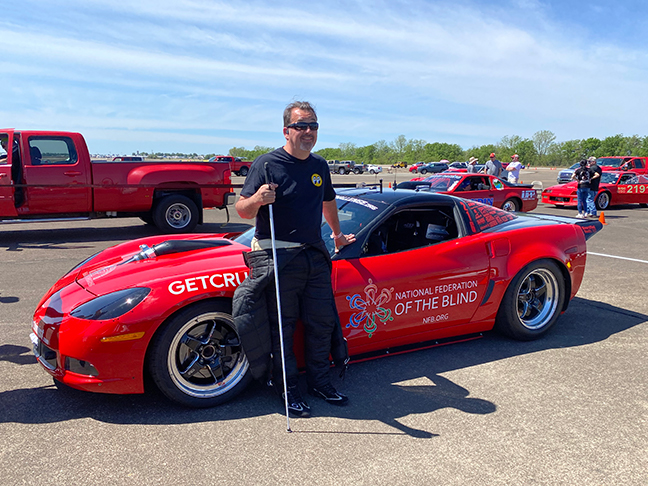 Dan stands with white cane next to his red C6 corvette.